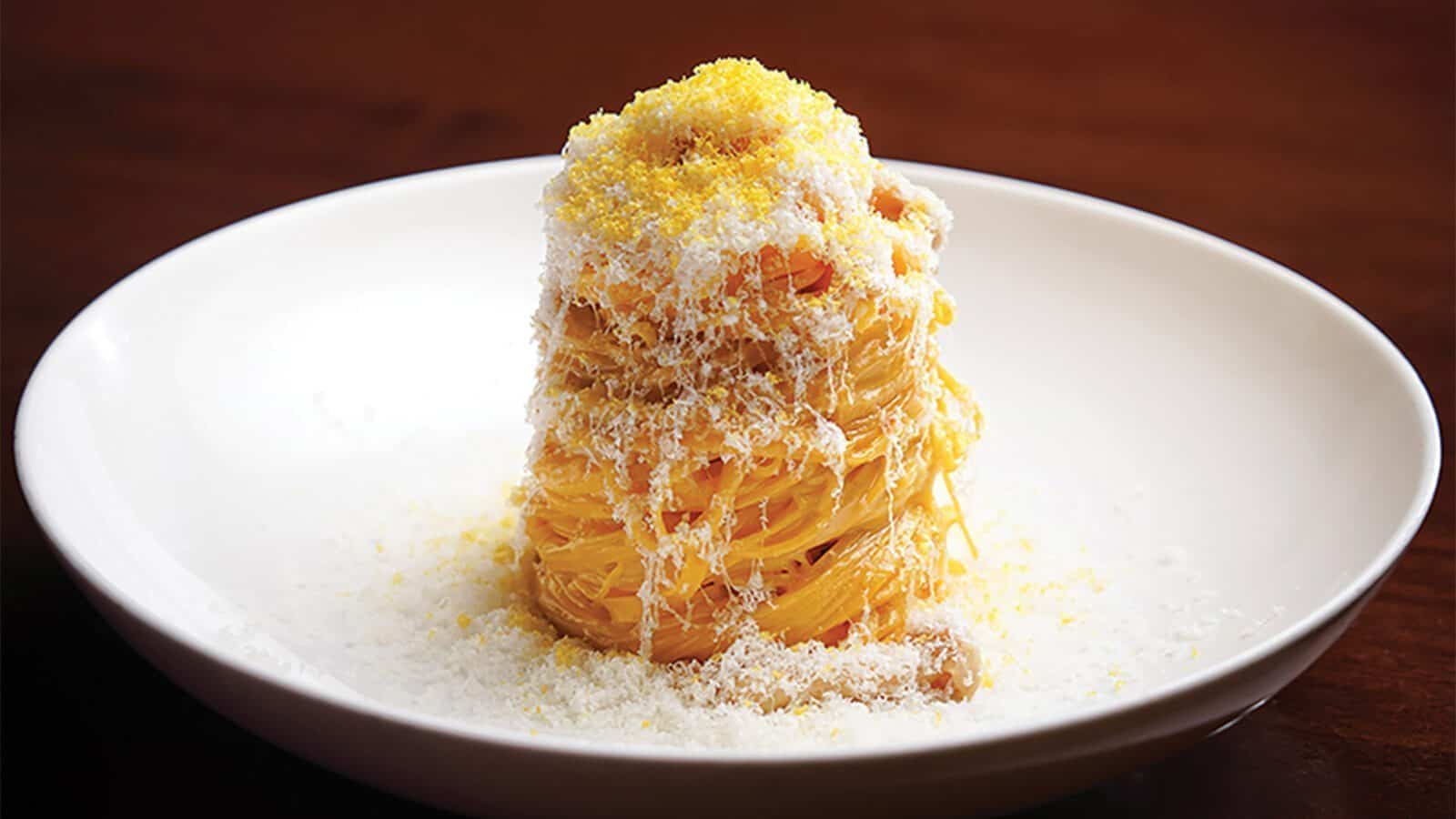A neatly twirled stack of spaghetti topped with grated cheese is served on a white plate against a dark background, promising a memorable meal worthy of any culinary getaway in British Columbia.
