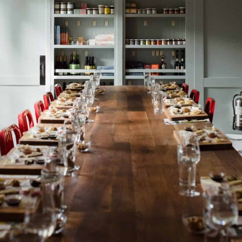 A long wooden table set for a meal with red chairs on each side, place settings, and food platters—perfect inspiration for your Seattle Father's Day gathering or browsing the ultimate Father’s Day gift guide. Shelves with jars and bottles are in the background.