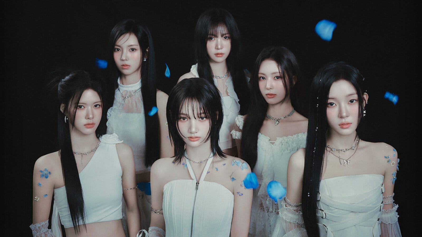 Six women in white outfits stand together against a black background with blue flower petals falling, evoking the elegance of UW and His Hollywood Career or the creative spirit Music Producer Kyu Lee talks Seattle.