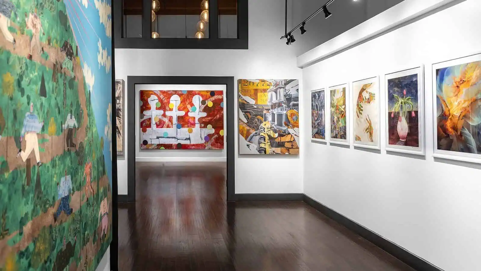 A contemporary art gallery displays colorful abstract and figurative paintings on white walls with a dark wood floor and modern lighting.