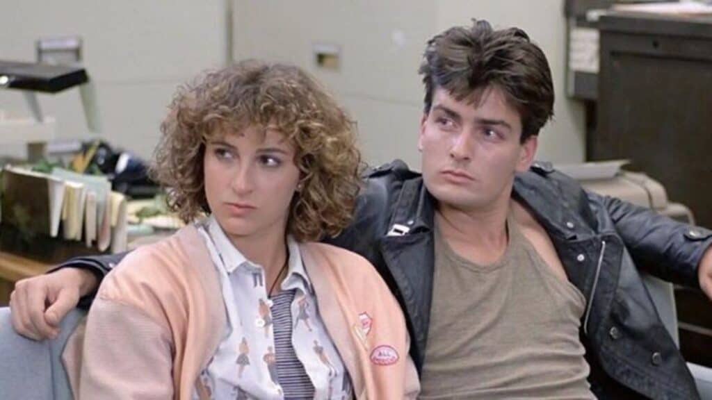A young woman and a young man sit closely together in an office setting, both looking slightly to the side with neutral expressions.