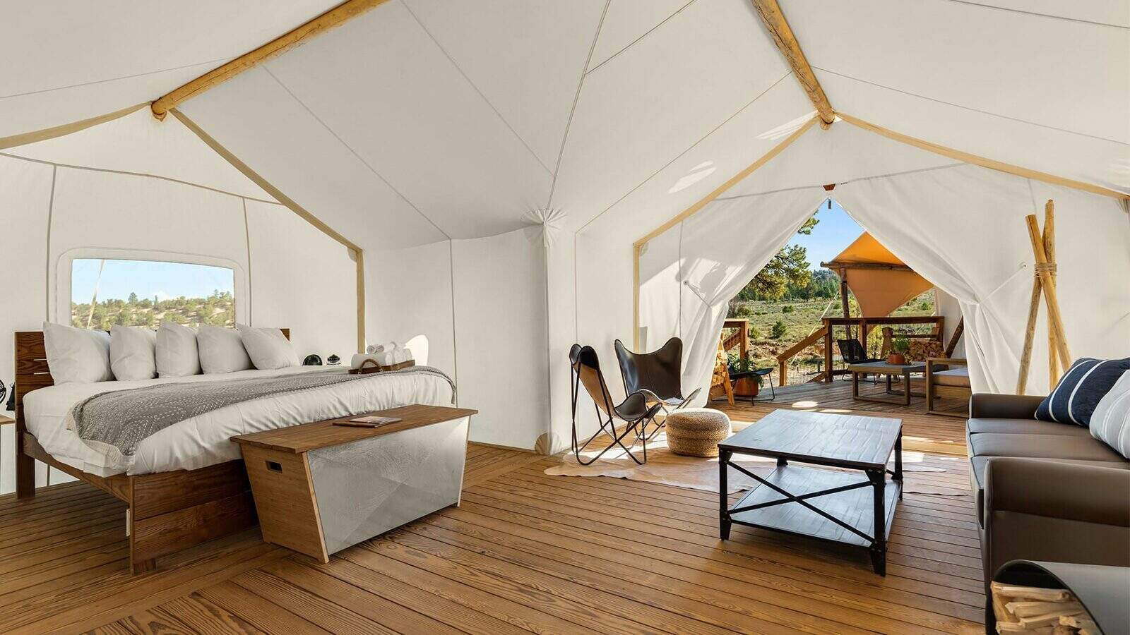Modern glamping tent interior at Gorge-ous Getaway with a bed, sofa, coffee table, and deck area, featuring wooden floors and natural light through open tent flaps.