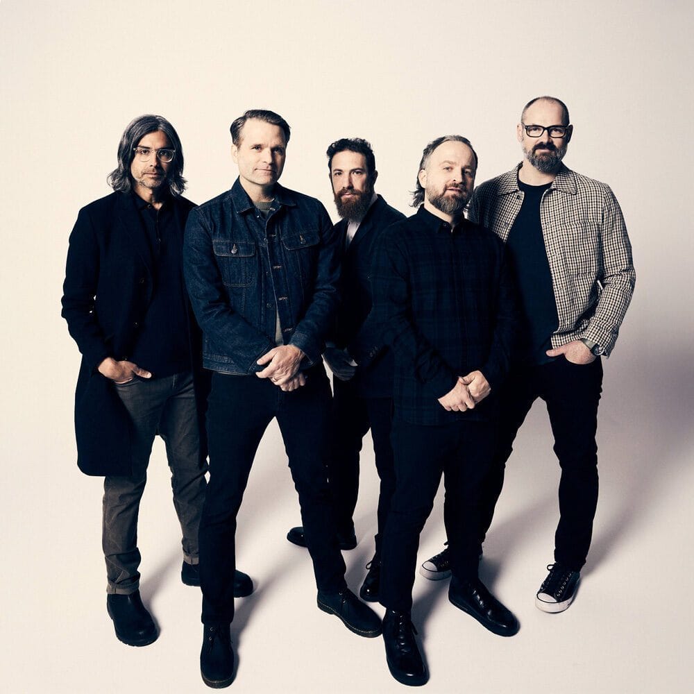Five men stand together against a plain white background, dressed in casual and semi-formal clothing, facing the camera—a Must List shot to remember on 07-31-2025.