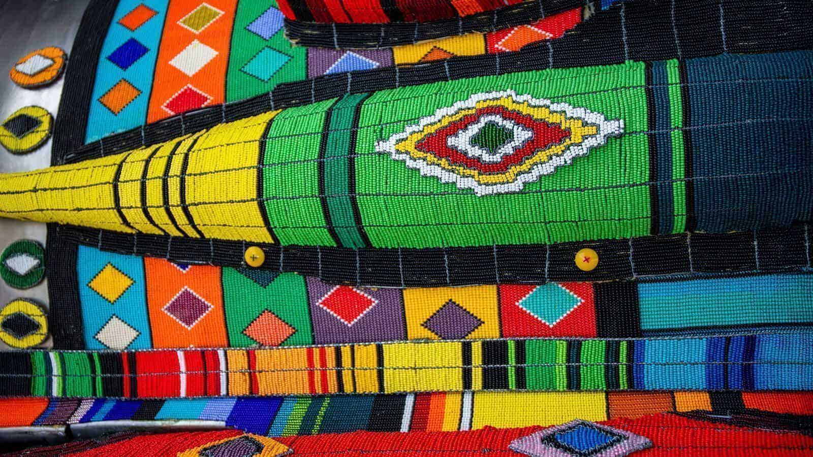 Close-up of a colorful beaded artwork with geometric patterns in green, yellow, red, blue, orange, and black—an expressive piece where art vividly tells stories of culture and war.
