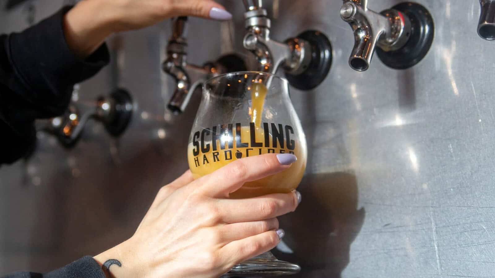 Schilling-HardCider_1600x900 A person fills a Schilling Hard Cider glass with a drink from a tap at a bar, celebrating the recent news that Thirteen Washington cideries win awards.