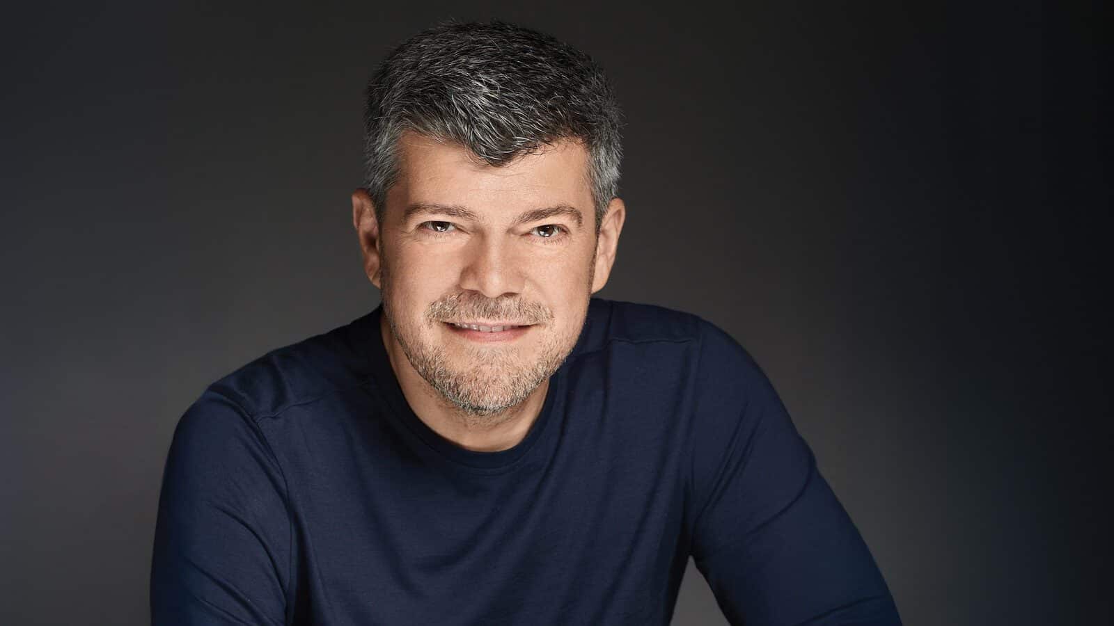 Dr. Nicolae Leca, M.D., a middle-aged man with short gray hair and a trimmed beard, is smiling and wearing a navy blue shirt against a plain dark background.