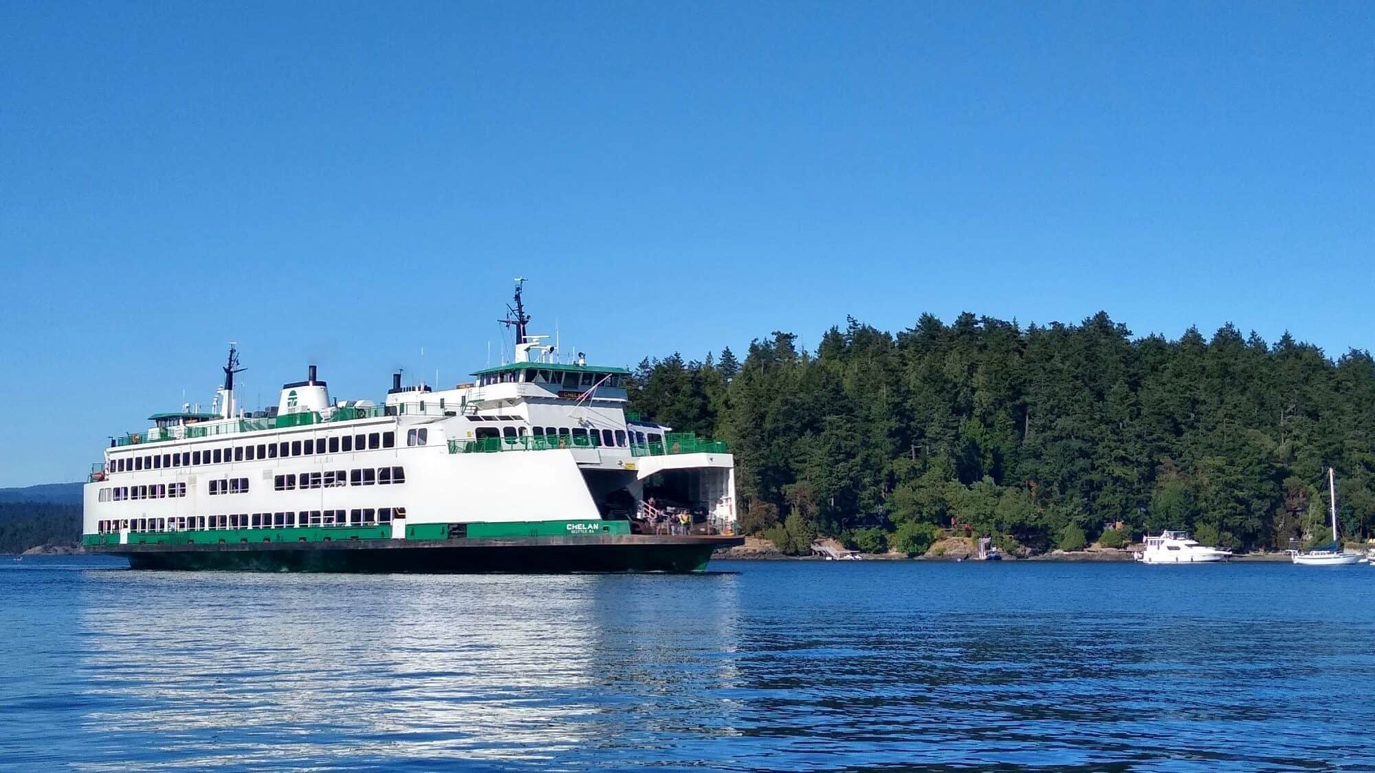 All Aboard! A large white and green ferry travels on calm water near a forested shoreline under a clear blue sky.