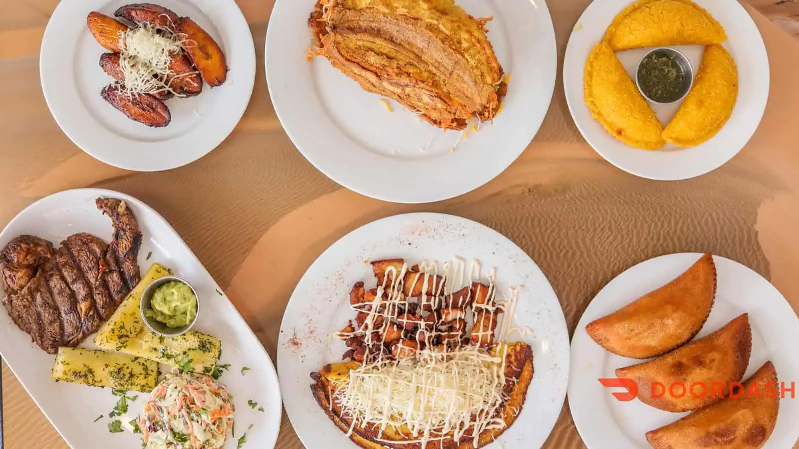 An overhead view of assorted Latin American dishes on white plates, including empanadas, grilled steak with sides, fried plantains, and enchiladas, celebrates Hispanic Heritage Month in Seattle—with a DoorDash logo in the corner.