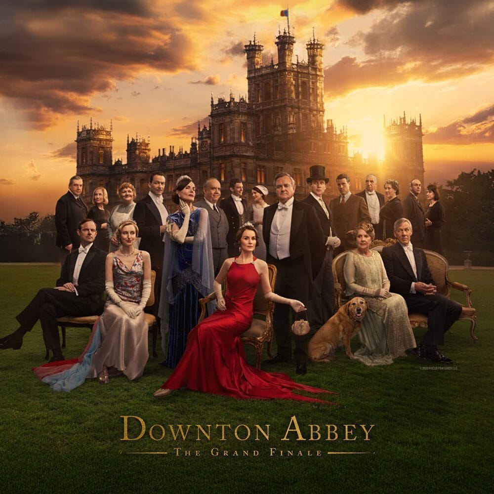 A large group of elegantly dressed people pose in front of a grand mansion at sunset, promoting "Downton Abbey: The Grand Finale"—a must list event premiering on 09-11-2025.