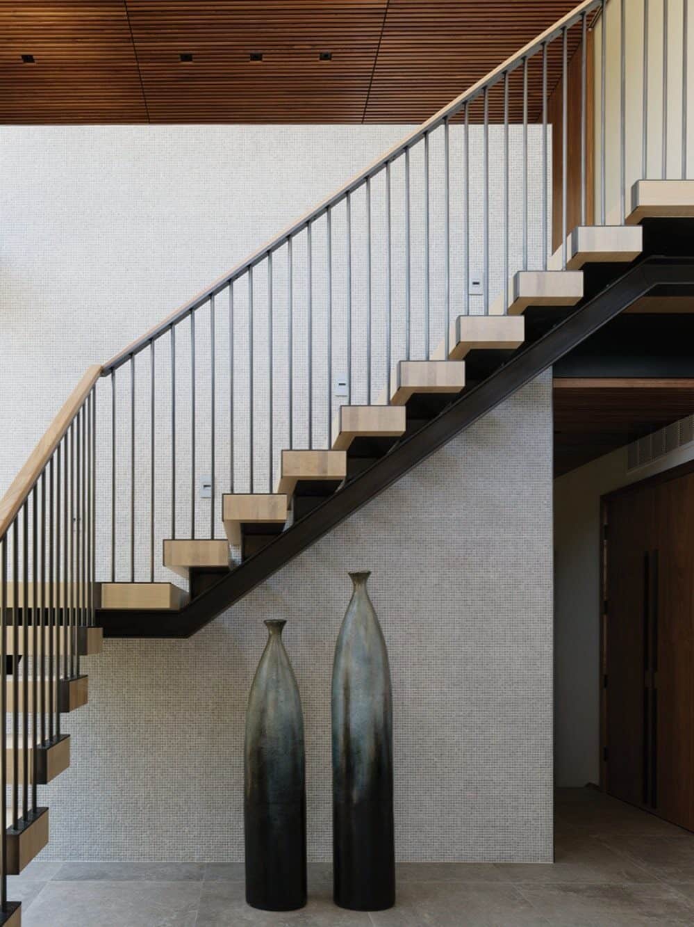 Modern staircase with wooden steps and metal railing, alongside two tall ceramic vases on a tiled floor below—an elegant touch that reflects the attention to detail found in custom-built homes.