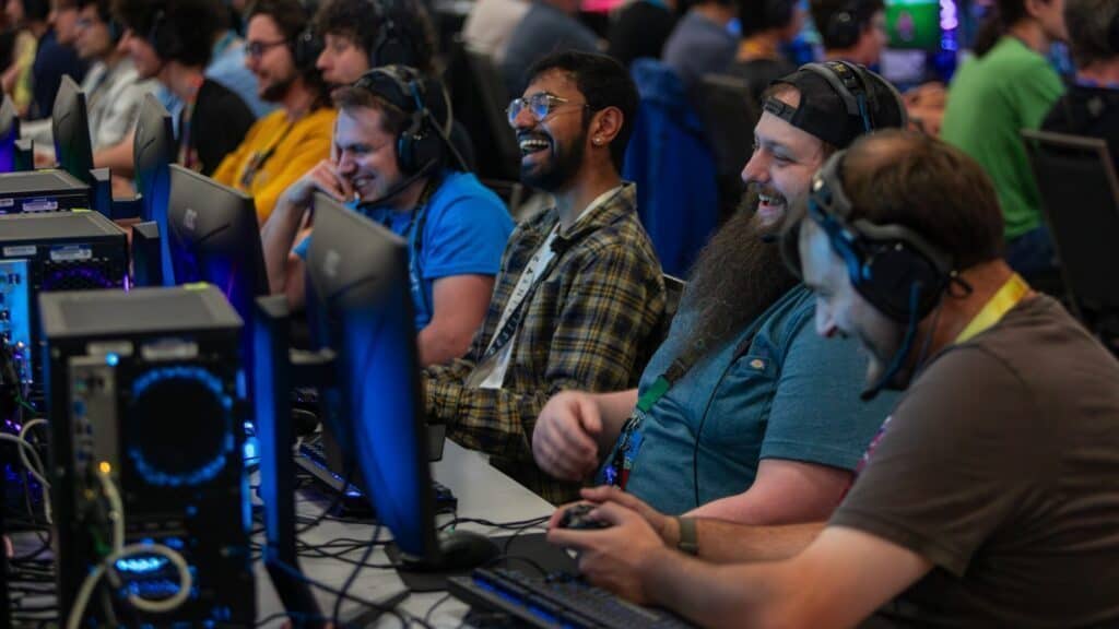 A group of people wearing headsets sit at computers, focused and smiling as they participate in a gaming event.