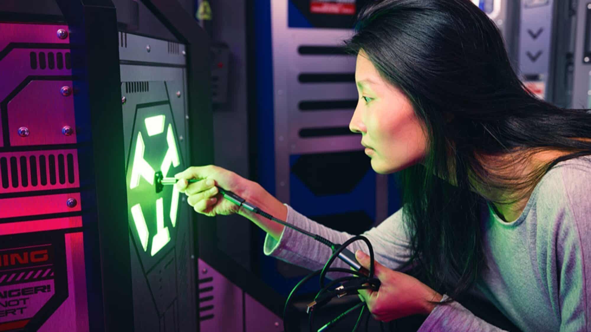 A woman inserts a cable into a panel with glowing green arrows in a futuristic, high-tech environment.