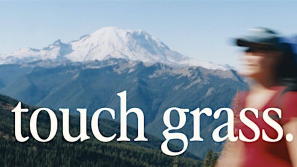 A blurred person in Seattle fashion stands before a mountain landscape, "touch grass." written across the image—capturing Pioneer Square’s outdoor spirit.