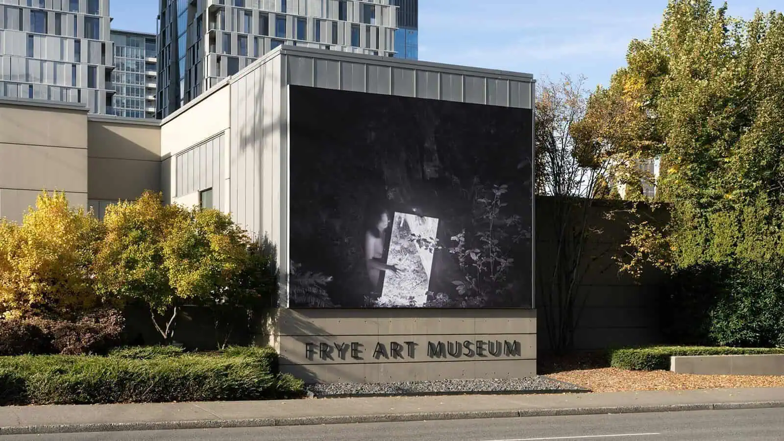 The Frye Art Museum offers free access to compelling art, with its exterior featuring a striking black-and-white photograph displayed on the building’s facade, surrounded by trees and urban buildings.