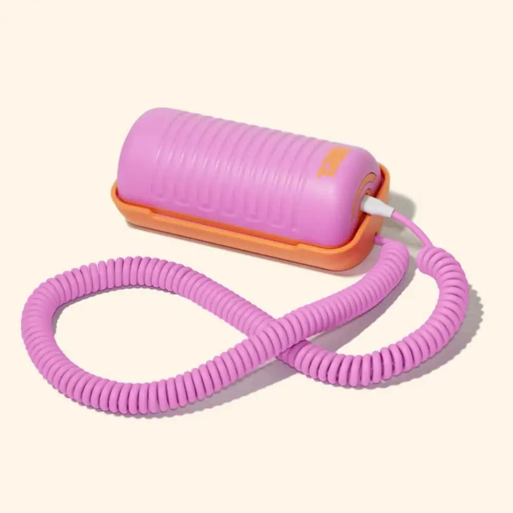 A pink, cylindrical landline receiver with a ribbed texture and a coiled cord is connected to an orange base, photographed on a beige background.