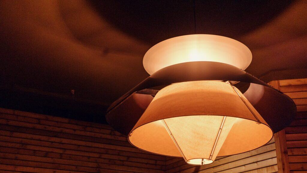 Modern ceiling light fixture with layered, geometric shades emitting a warm glow in a room with wooden panel walls.