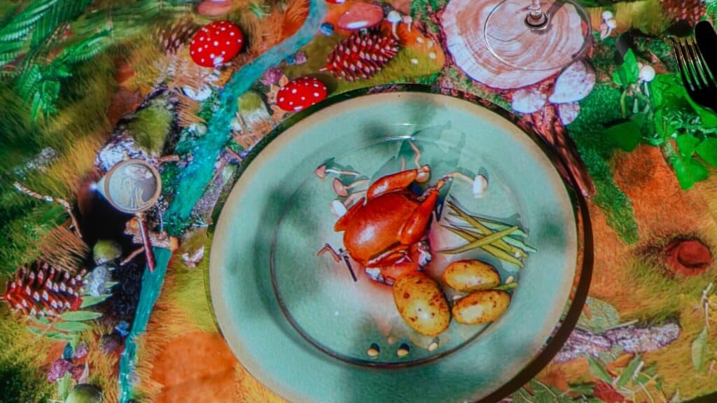 A plate with roasted chicken, potatoes, and green beans on a table featuring a colorful forest-themed tablecloth with mushrooms and pinecones.