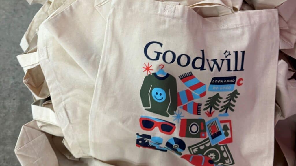 A canvas tote bag with the Goodwill logo, decorated with illustrations of clothing, accessories, and the words "Look Good, Do Good.