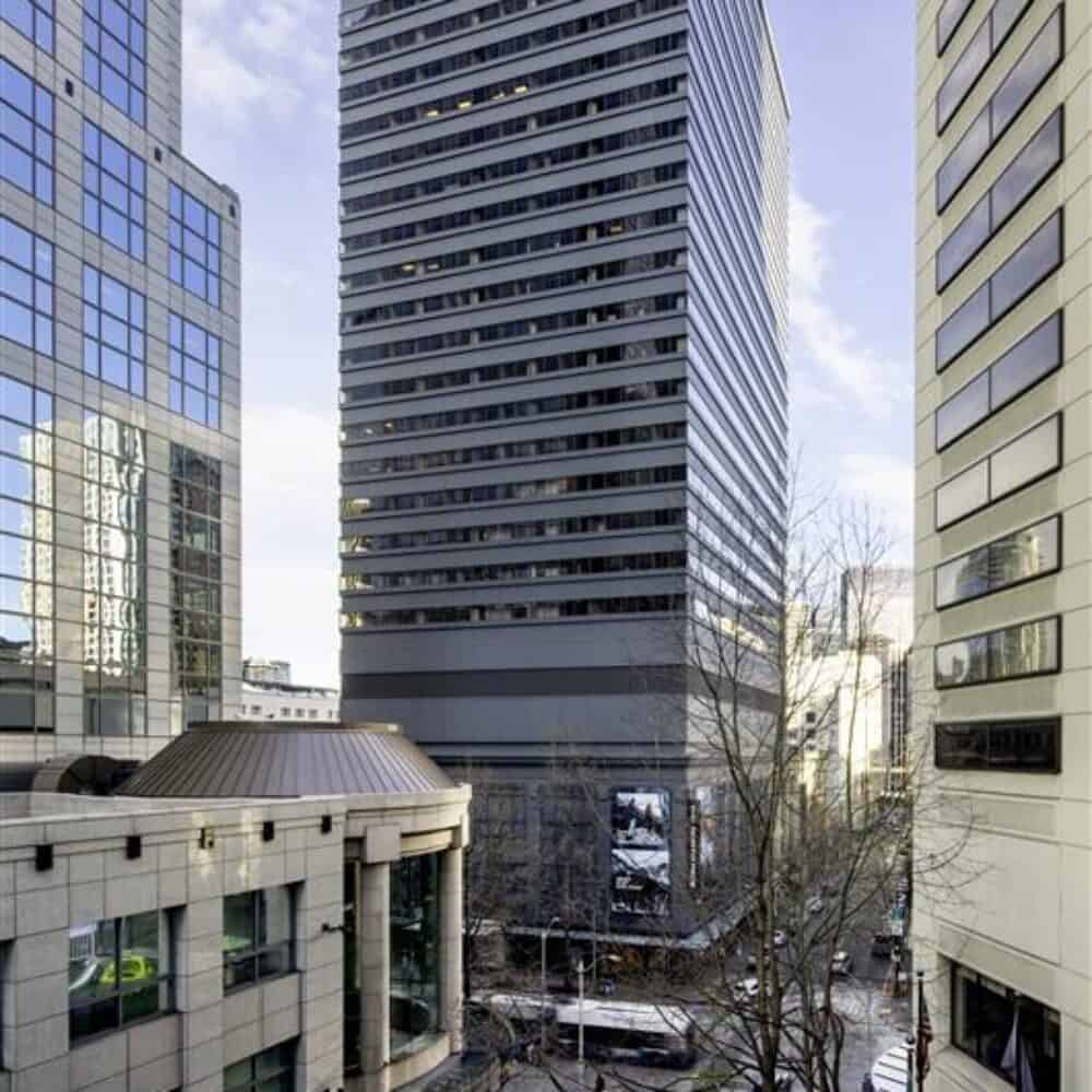 Tall modern office buildings surround a busy downtown street, where cars pass by leafless trees and the nearby Barnes & Noble on a clear day.