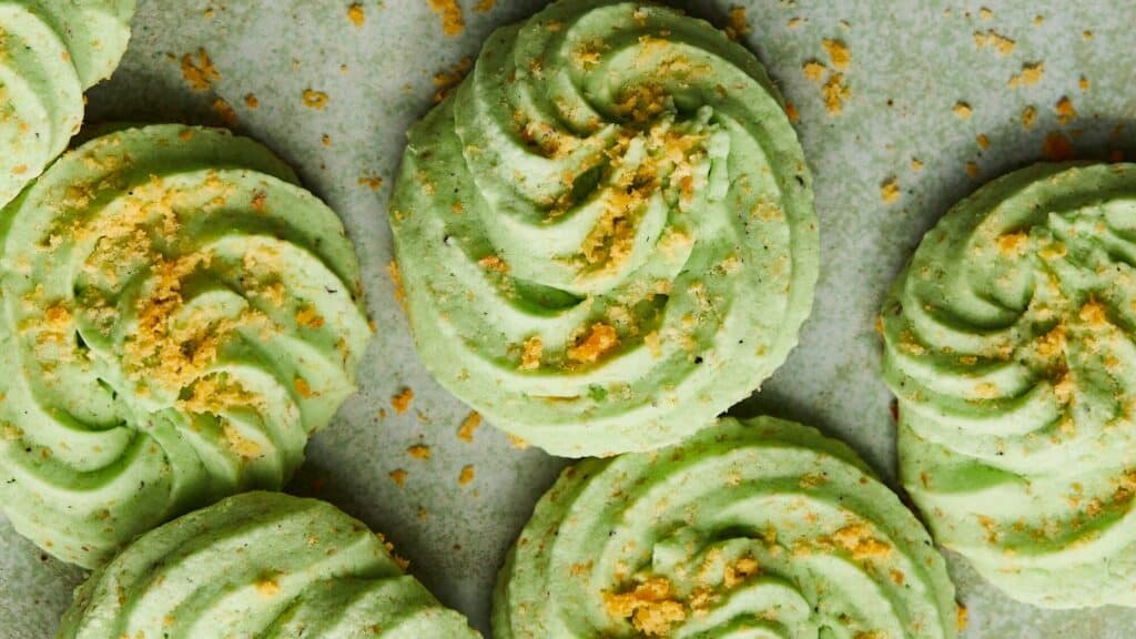 Green swirled cookies with crumbly golden topping arranged on a gray surface.