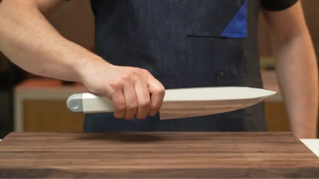 A person in a dark apron holds a large kitchen knife over a wooden cutting board, preparing to cut.