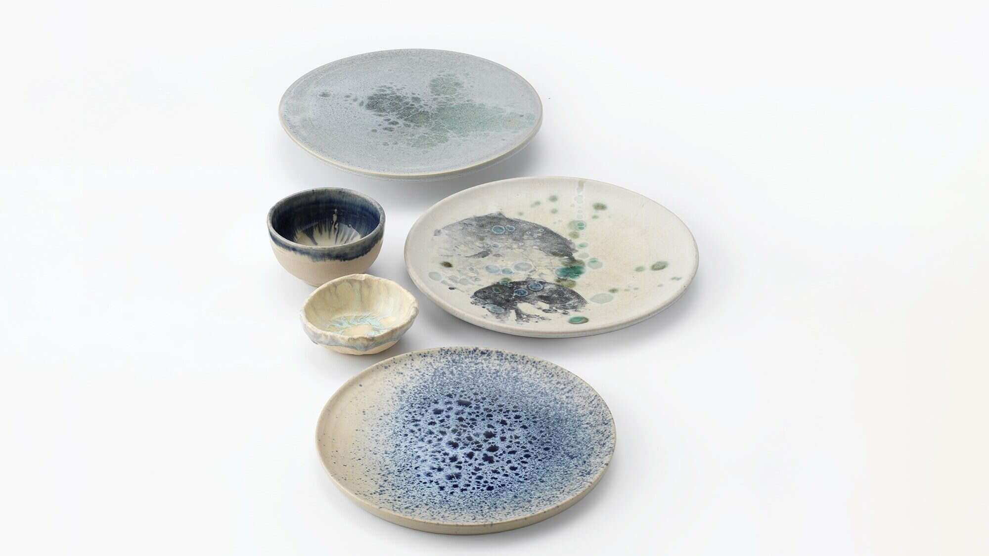 Five ceramic dishes and cups with abstract blue, green, and gray glaze patterns—your Fave Five Little Escapes—arranged on a white background.