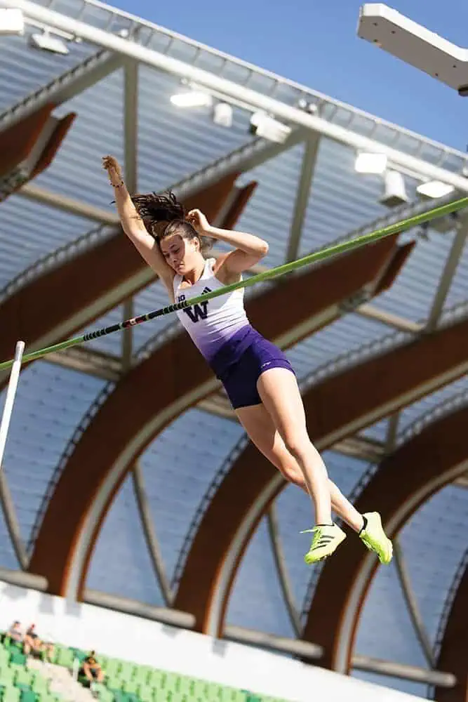 Amanda and Hana Moll, renowned pole vault champions from UW Track and Field, soar mid-air as they clear the bar during an outdoor stadium event.