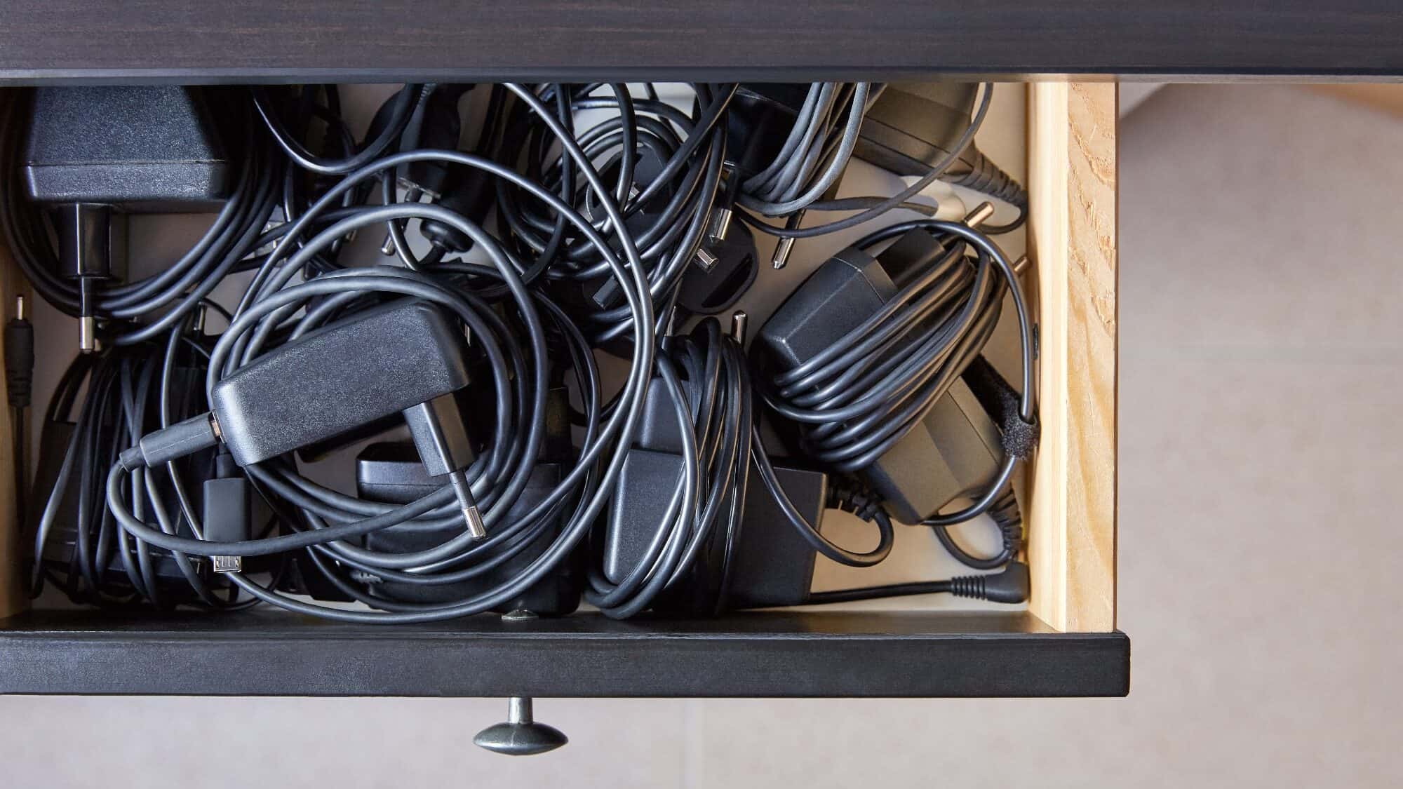 Drawer filled with tangled black cords, cables, and power adapters.