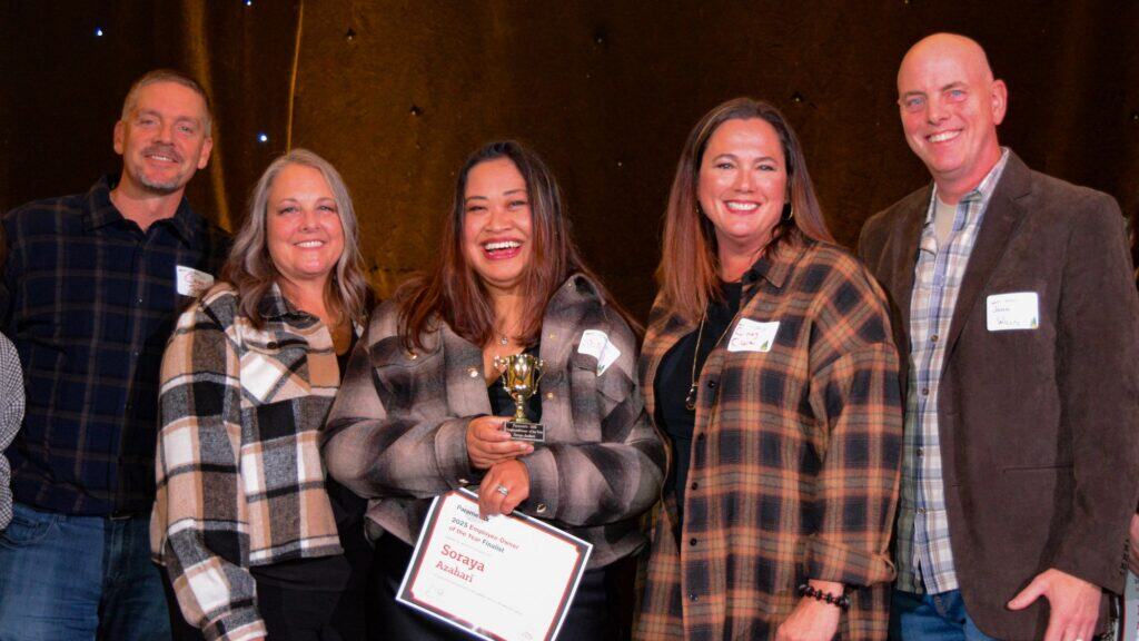 Five people stand together smiling; the woman in the center holds a trophy and a certificate with the name "Soraya," indicating she has received an award.