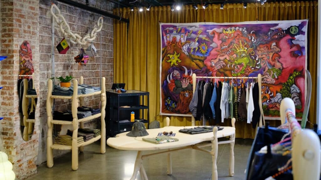 Clothing store interior in Portland’s Pearl District featuring an abstract tapestry, racks of clothes, light wooden furniture, a brick wall, and yellow curtains—a true wanderer’s guide to style.