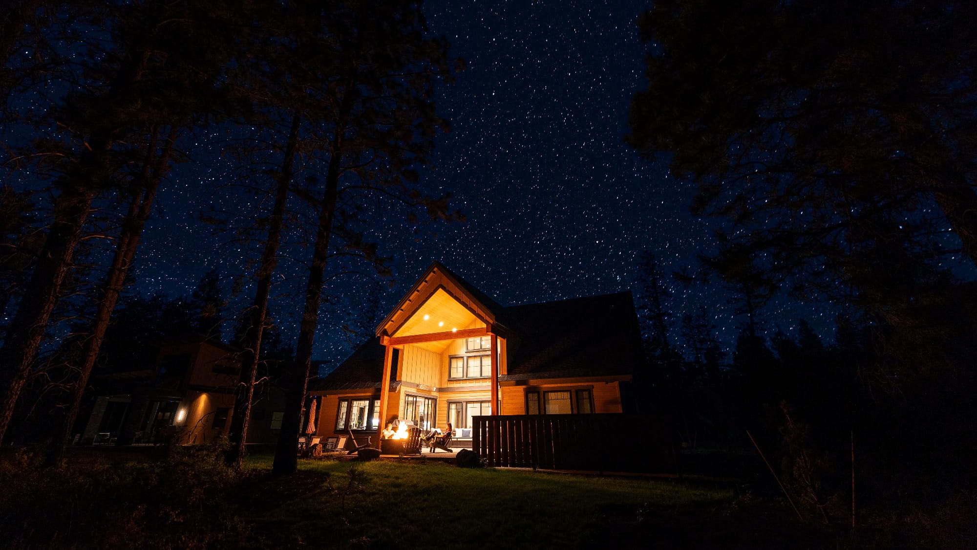 A warmly lit wooden house sits among tall trees on Suncadia land, glowing beneath a clear, star-filled night sky.