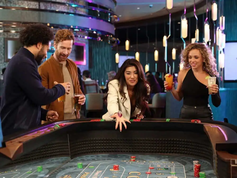 Four people stand around a casino craps table, holding drinks and watching as a woman in a white jacket throws dice—capturing the excitement of a night out like nowhere else.