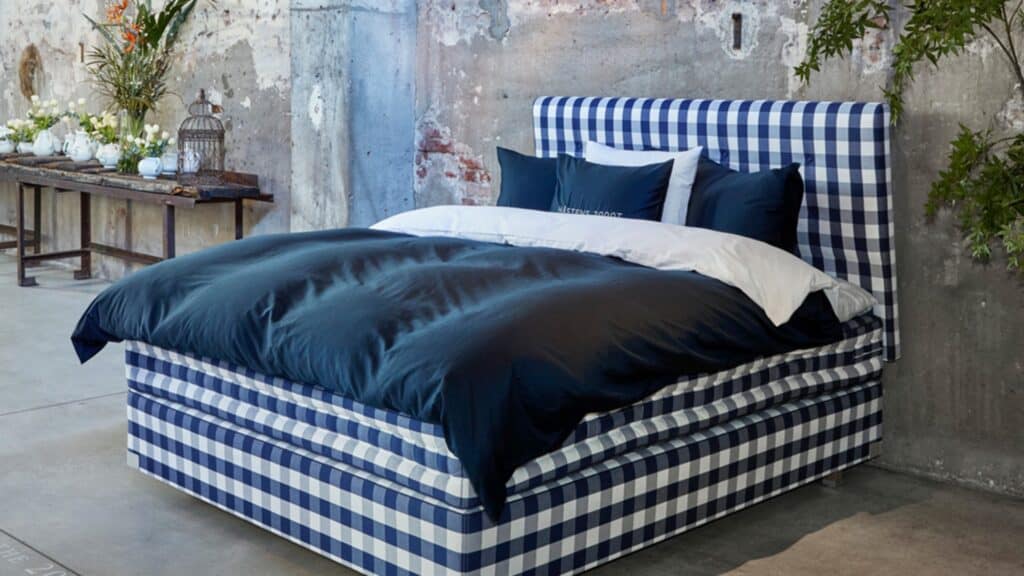 A bed with a blue and white checkered frame and headboard, navy bedding, and white pillows, positioned against a concrete wall in an industrial-style room.