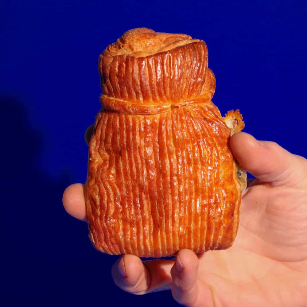 A hand holding a rectangular, golden-brown pastry with vertical ridges, set against a solid blue background.