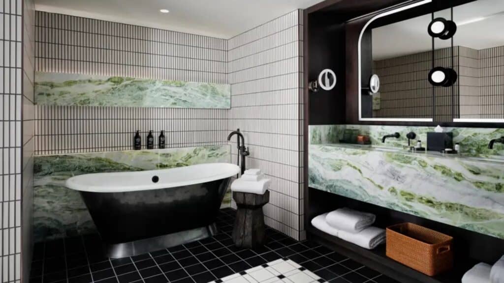 Modern bathroom with a black freestanding tub, green marble surfaces, sleek black fixtures, and tiled walls—perfect for relaxing getaways or unwinding after Lunar New Year celebrations. Towels and toiletries are neatly arranged.