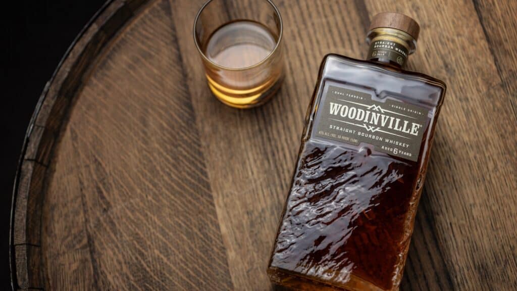 A bottle of Woodinville Straight Bourbon Whiskey and a glass with whiskey sit on a wooden barrel.