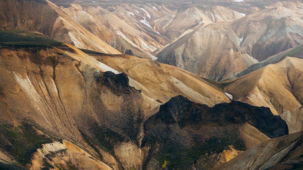 Layered, multicolored mountain ridges with patches of snow and sparse vegetation, creating a striking natural landscape.