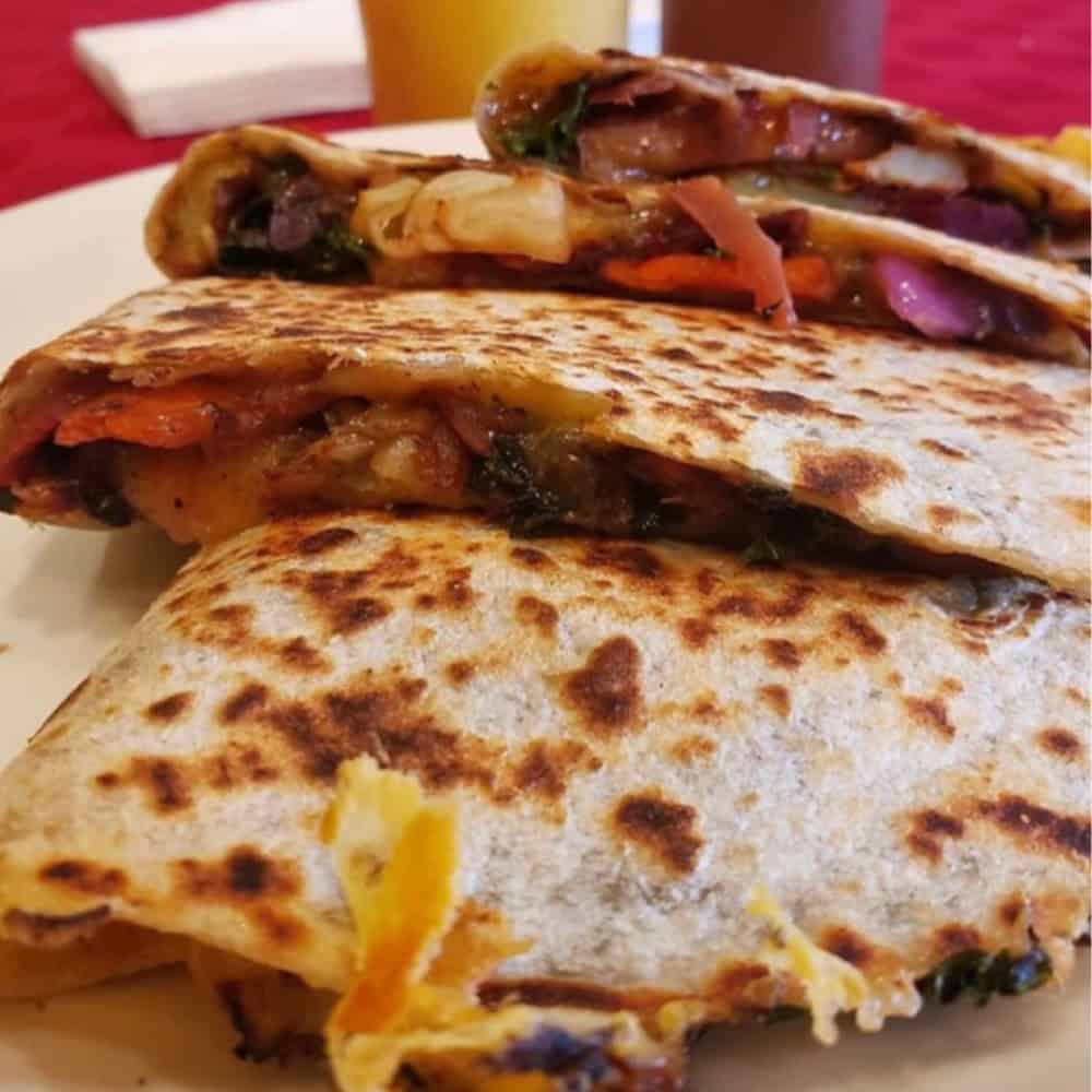 Close-up of three grilled quesadillas filled with vegetables and melted cheese, stacked on a white plate with a red tablecloth in the background.