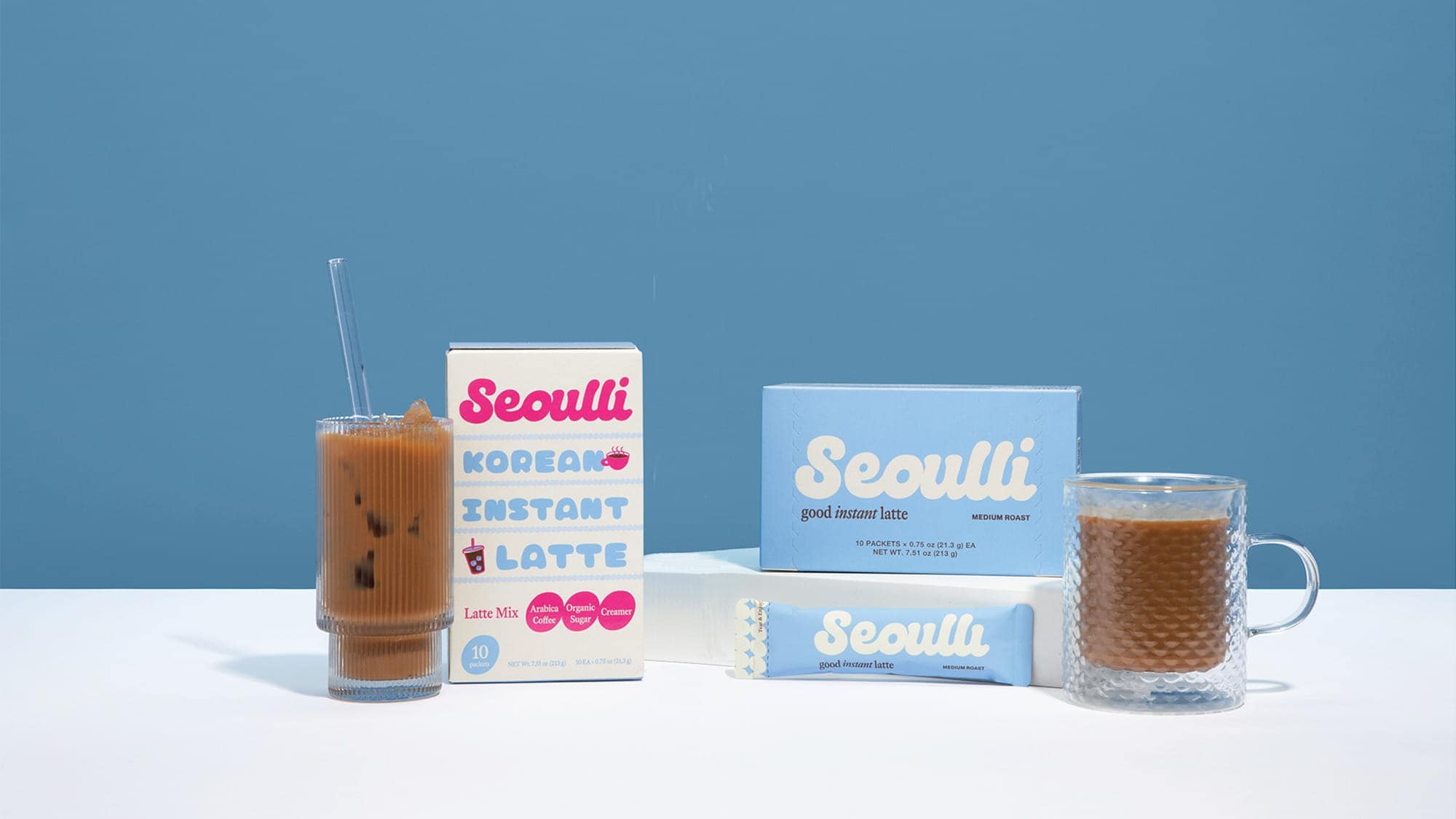 Two glasses of iced and hot coffee are placed next to Seoulli Korean instant latte packaging against a blue background, perfect for a midday break or brainstorming session on women in leadership.