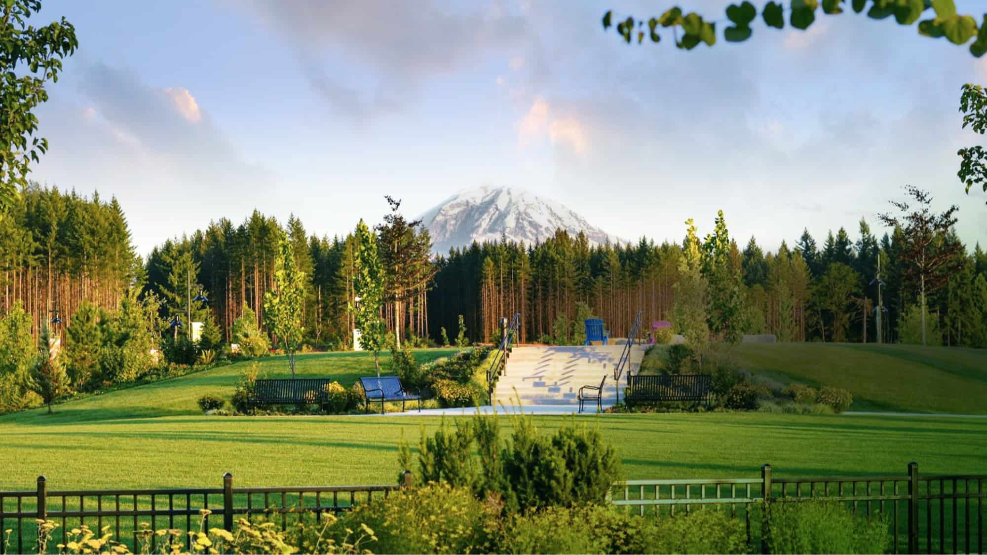 A landscaped park with green lawns, benches, trees, and a staircase, with a snow-capped mountain and blue sky in the background.