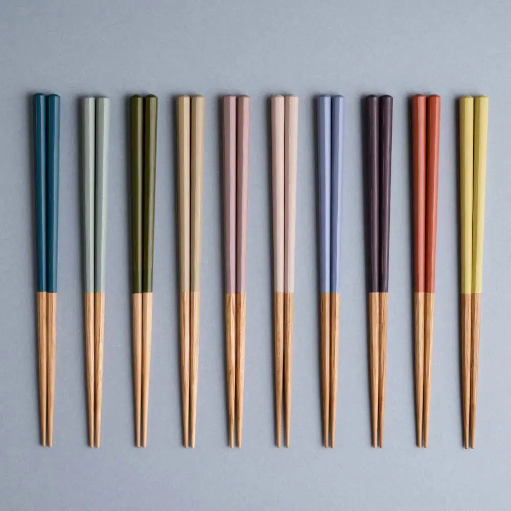 Ten pairs of chopsticks with wooden tips and colorful handles are arranged vertically in a row on a gray background.
