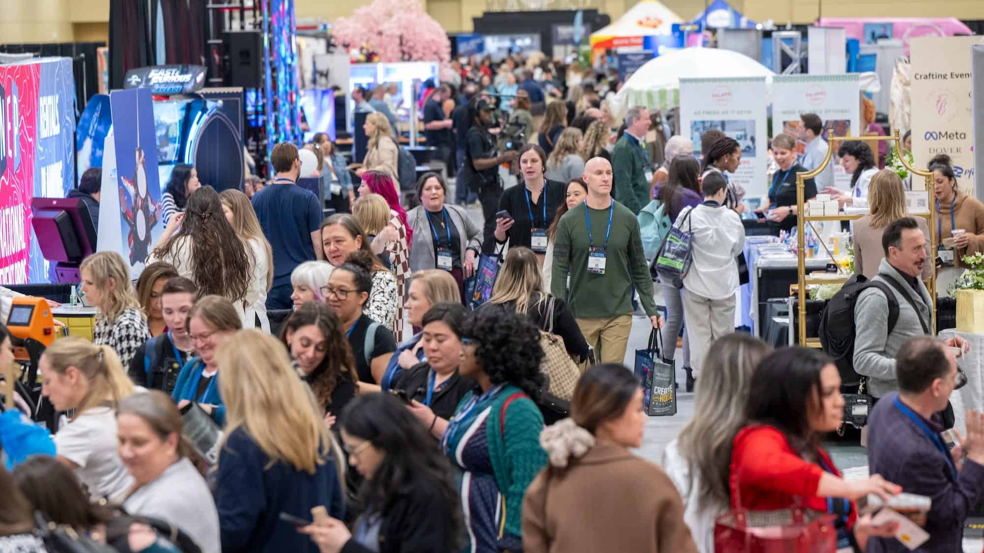 A large crowd of people walks through and gathers at various booths in a busy exhibition hall, making it easy for event planners Seattle to find vendors Seattle for their next big occasion.