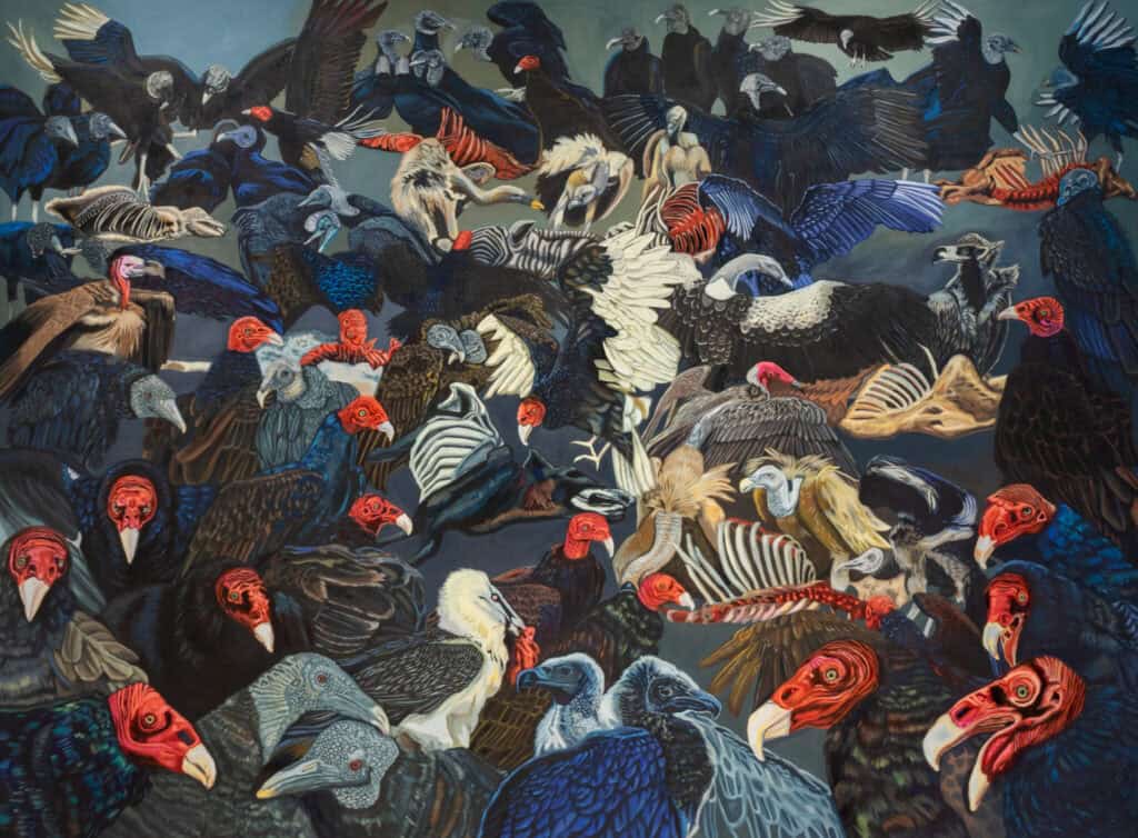 A dense flock of vultures with red and black heads gather closely together, some with wings outstretched, against a subdued background.