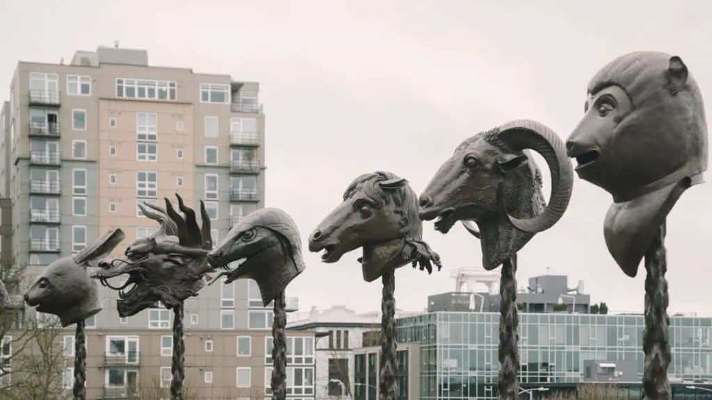 A row of bronze animal head sculptures, including a dragon, horse, and ram, displayed outdoors with modern apartment buildings in the background.