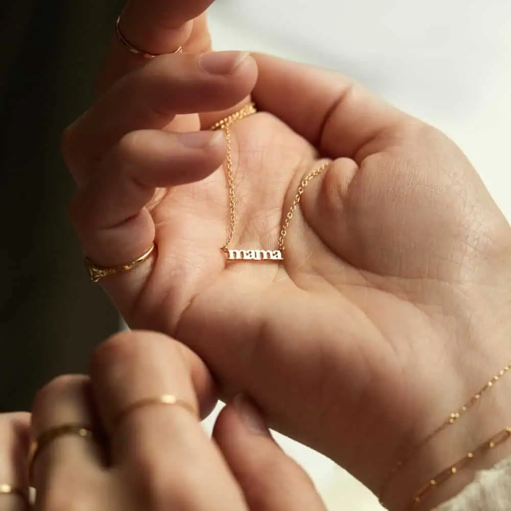 A person holding a gold necklace with a pendant that spells "mama" in lowercase letters—a perfect Mother’s Day Gift.