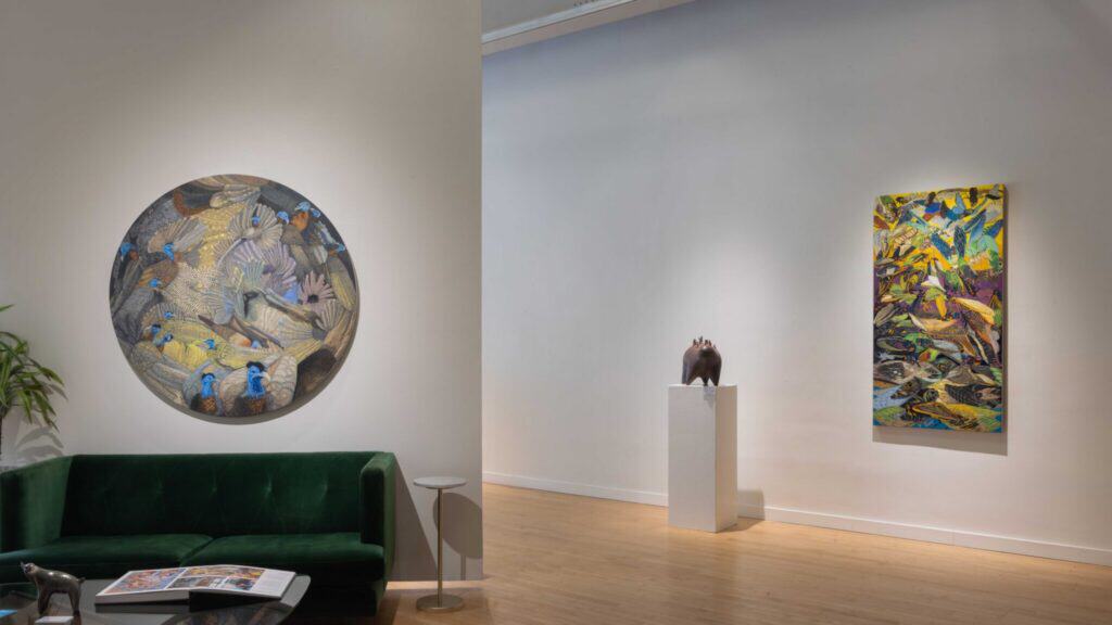 Art gallery interior with a green sofa, a round painting on the left wall, a colorful rectangular painting on the right wall, and a small sculpture on a pedestal in between.