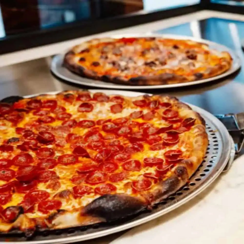 Two large pizzas on metal trays, one topped with pepperoni slices and the other with mixed toppings, showcased on a counter—perfect examples of what you’ll find at some of the best pizza Seattle has to offer.