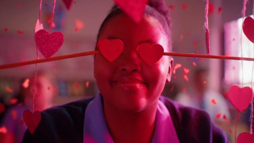 A person smiles with red heart shapes over their eyes, held by a pencil. Pink and red decorations hang around them in a festive setting, capturing the excitement of the SIFF film festival.