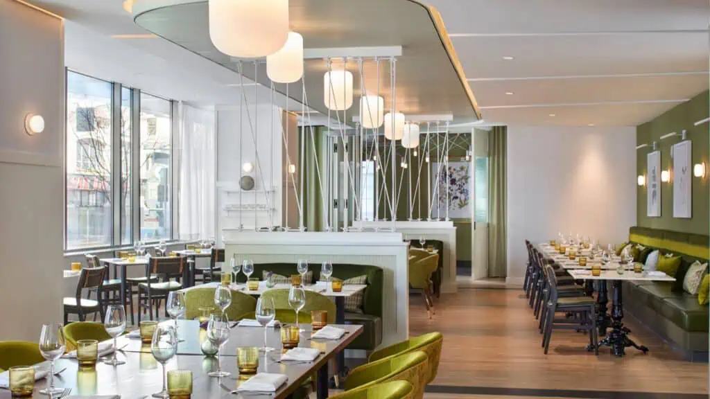 Modern restaurant dining area with green and white decor, set tables with glassware, large windows, and pendant lighting—perfect for savoring signature Lobster Rolls before catching a SIFF screening nearby.