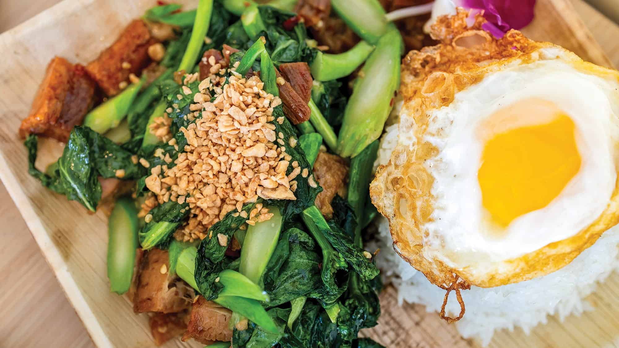A plate of rice topped with a sunny-side-up fried egg, sautéed greens with chopped peanuts, and pieces of cooked meat—a perfect example of Seattle fusion Thai cuisine at Bloom Thai in Lakewood.